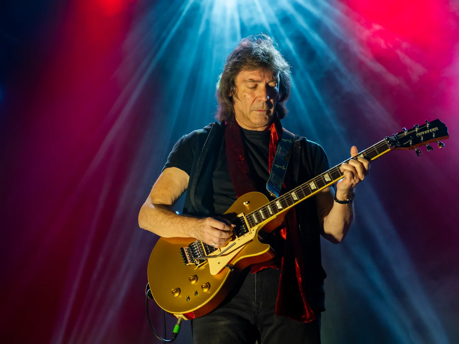 Steve Hackett playing guitar under blue and red stage lights at Eventim Apollo in 2014